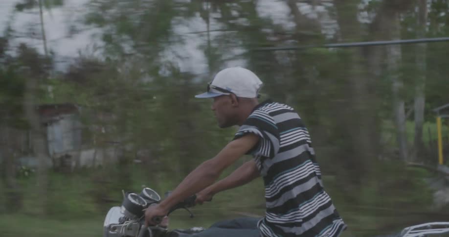 A man in a striped shirt drives a motorcycle