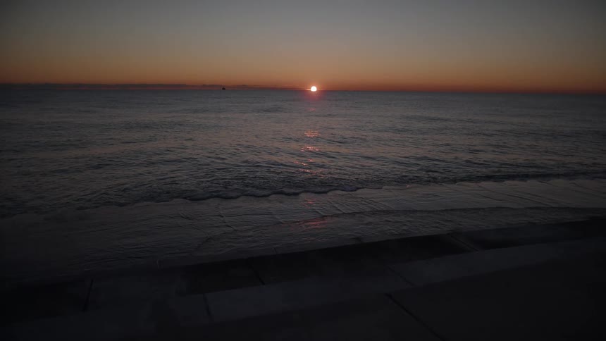 Waves roll onto a beach near a concrete barrier area at sunset