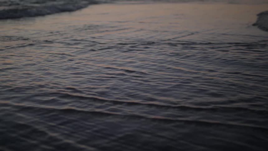 Waves crash onto the beach shore in the evening