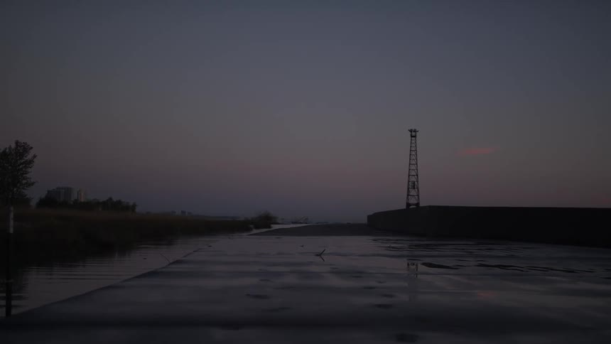 A radio tower is by the water at dusk