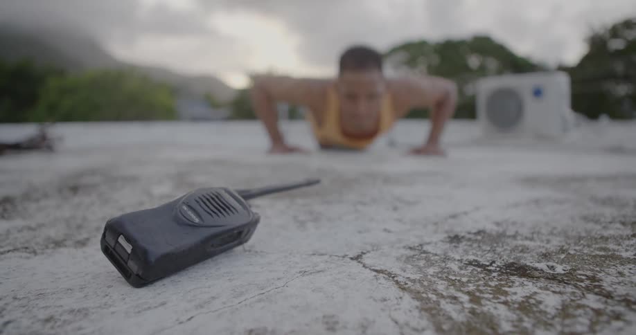 Man doing push ups on a hard surface outdoors with a two-way radio in the foreground