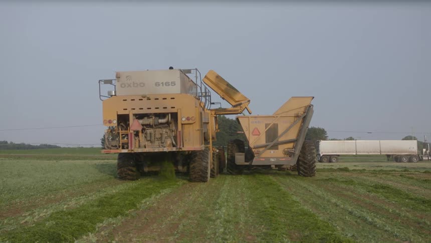The farm vehicle is traveling along the long farm field