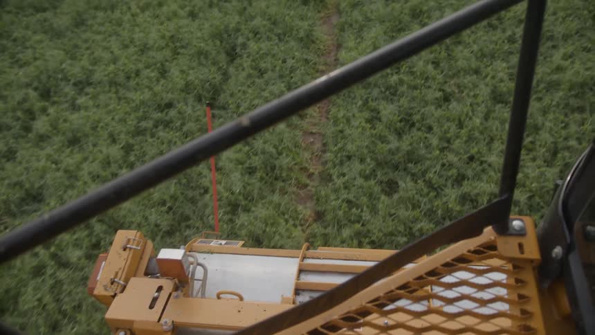 The combine harvesters cutting mechanism actively moves through a vibrant green field creating a distinct path as it operates