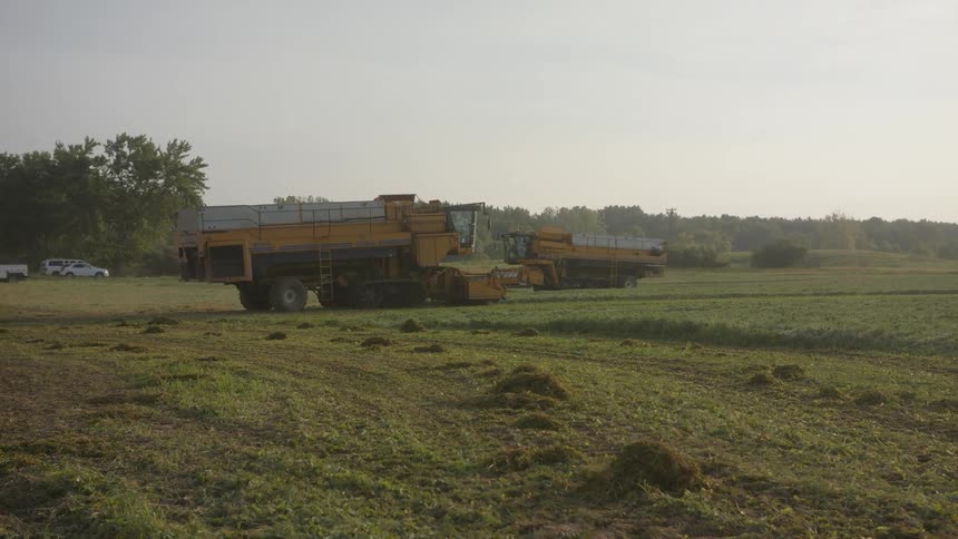 The farm vehicles are working the field on a hazy day
