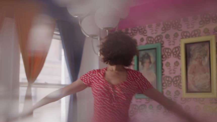 Woman in a red dress dances in a colorful room with decorated walls