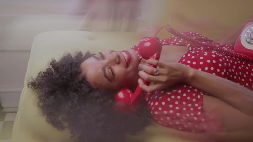Smiling woman in a red polka dot dress talks on a retro rotary phone