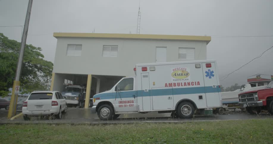 An ambulance is parked in front of a building while it rains