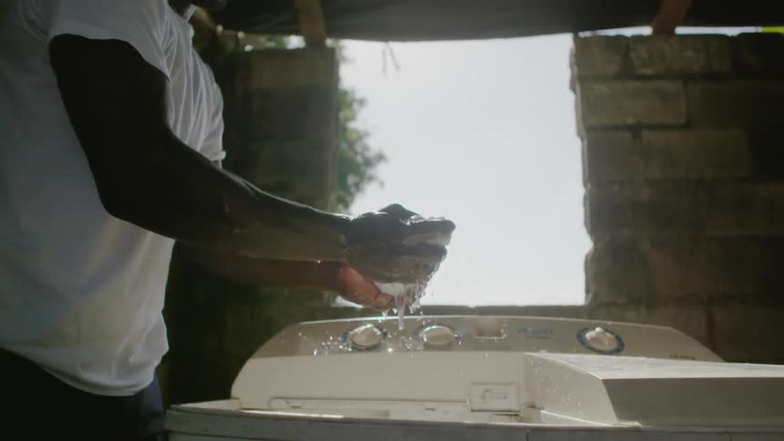 A man wrings out a piece of cloth over a washer