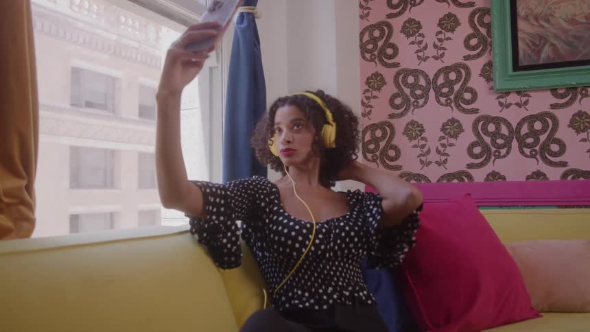 A woman wearing headphones is making kissing faces as she takes selfies with her phone