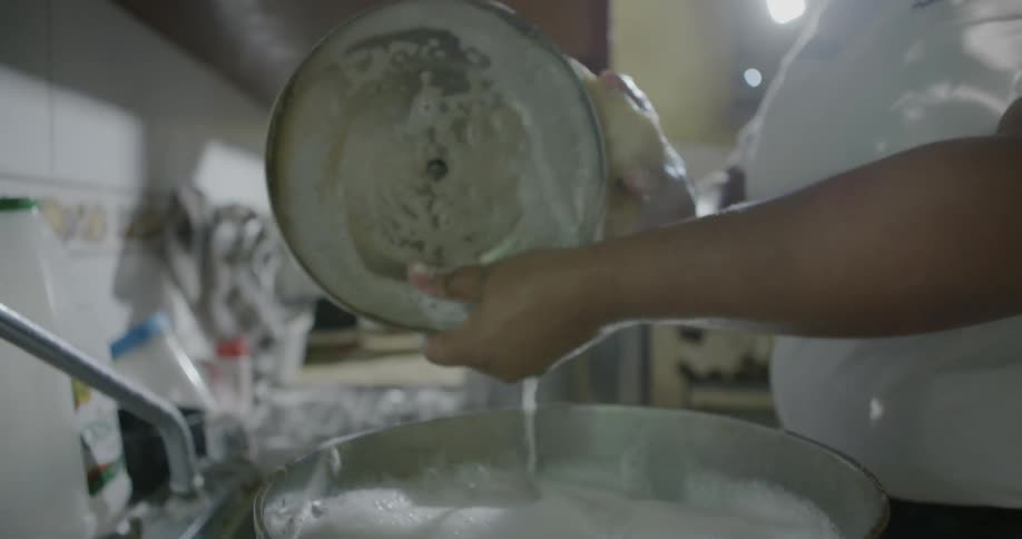 A woman washes a pot in a kitchen sink