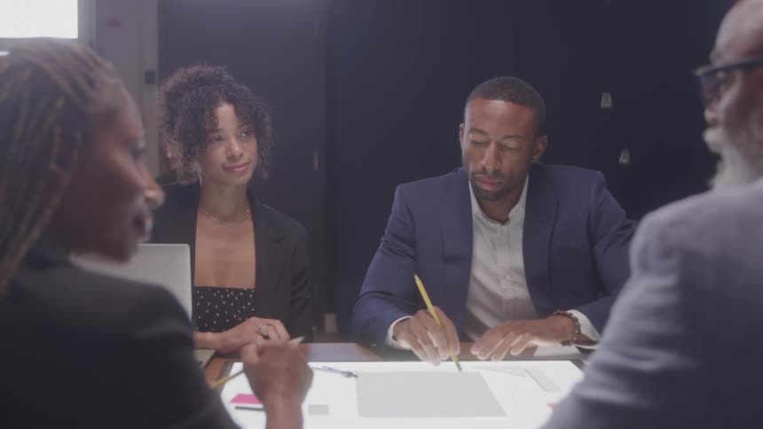 Four people are sitting at a table with electronics and having a discussion