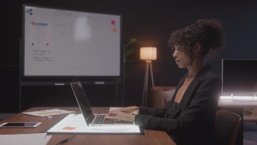 A woman is sitting at a desk typing on a laptop