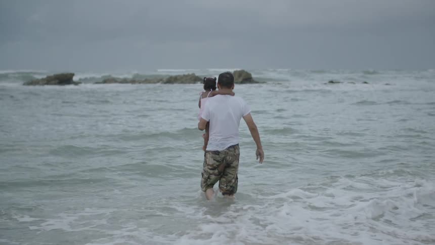 A man carrying a girl wades into the ocean