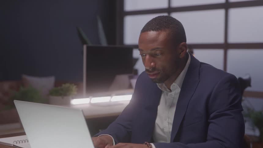 Man in a suit typing on a laptop in a modern office