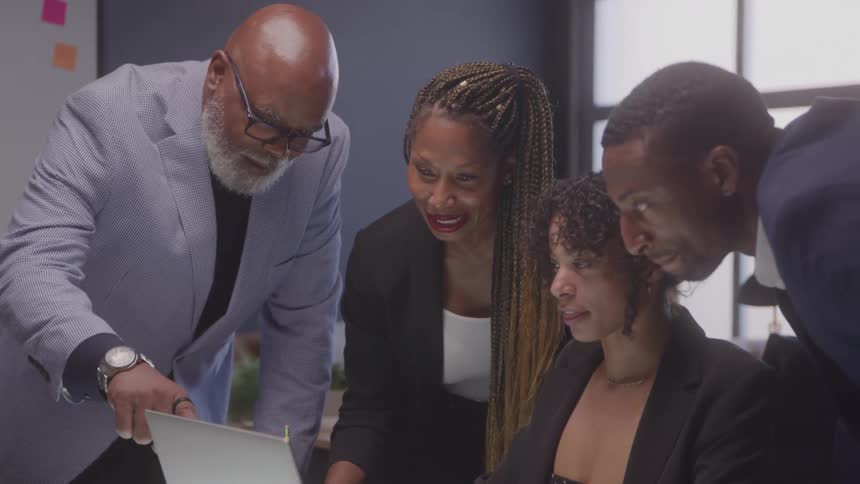 Four people around a laptop at an office table