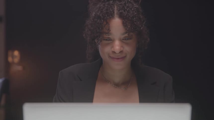Woman in a black blazer looking at her laptop screen with a focused expression