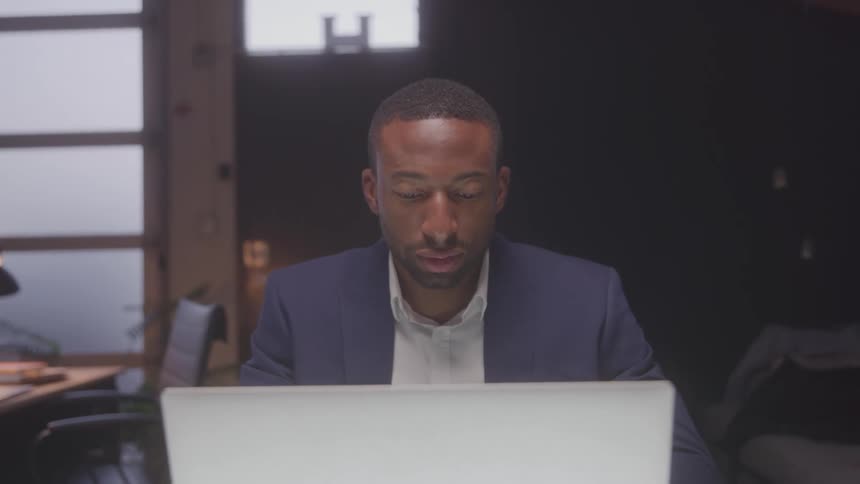 Man in a blue suit and white shirt staring intently at his laptop screen
