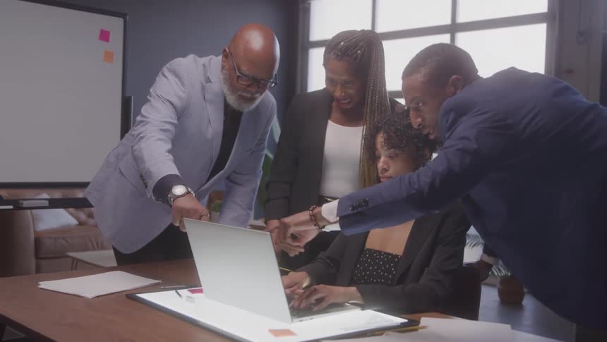 Four coworkers gathered around a laptop collaborating on a task in the office