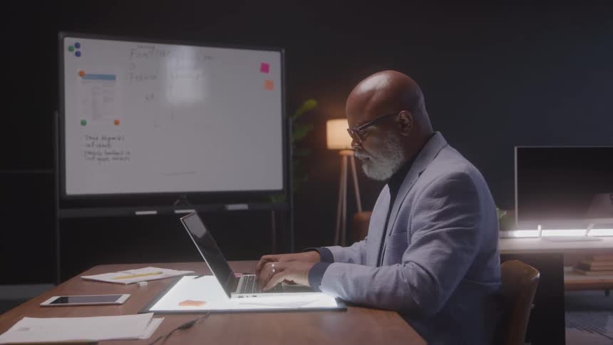 Close up of a middle aged black man working at a desk with a laptop in an office