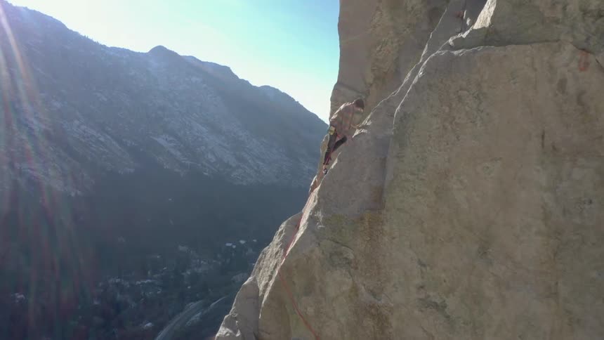 A female mountain climber ascends a rocky mountain in the wild at midday
