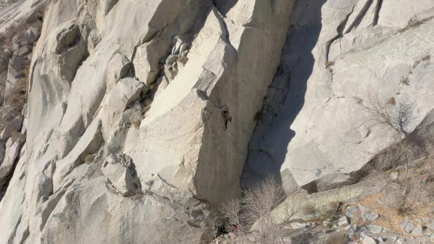 A mountain climber continues ascending a rocky mountain in the wild on a sunny day
