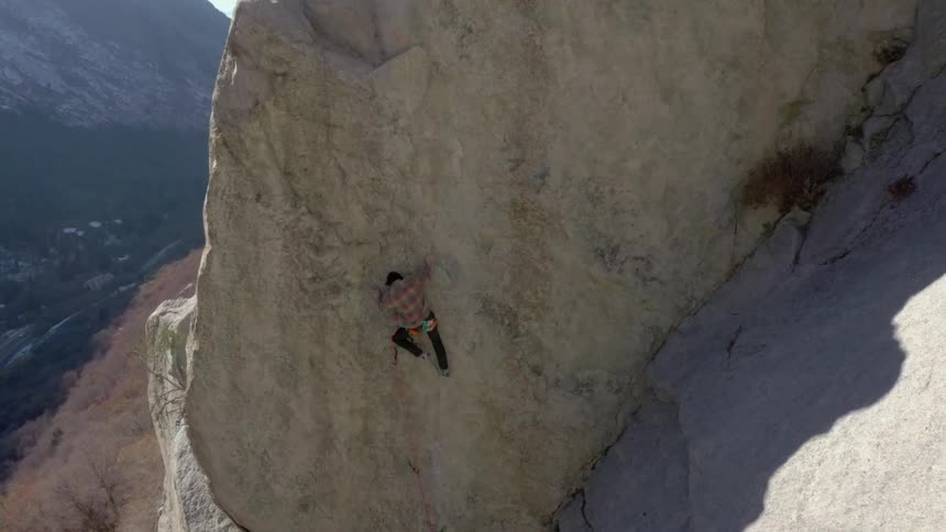 Person climbing a mountain wall with a safety harness