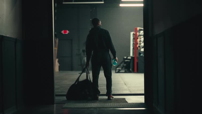 A young black man drops his bag while standing at a gym room entrance