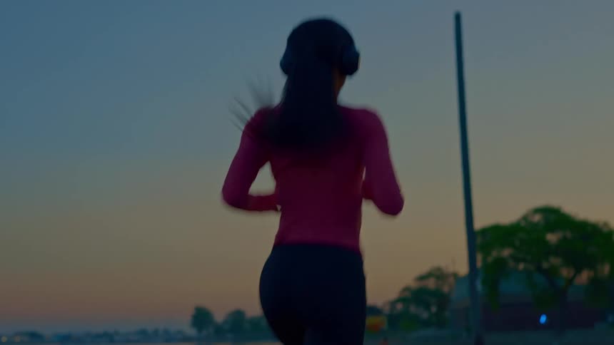 Woman runs by the water at sunset wearing headphones