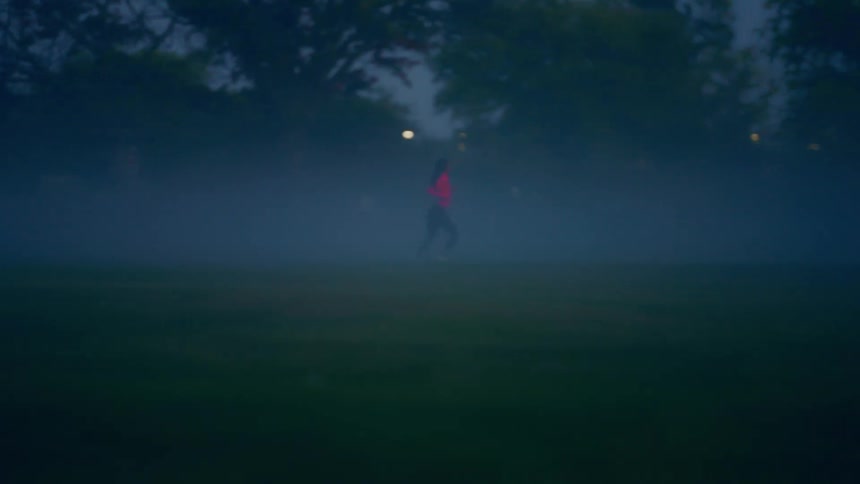 A young woman jogs across a field outdoors at dusk during a foggy day