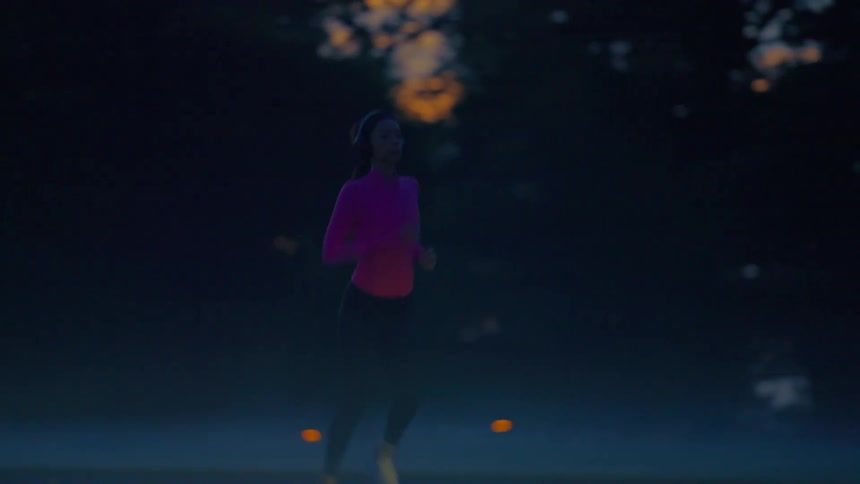 A young black woman jogs on an empty street outdoors during a foggy day at sunset