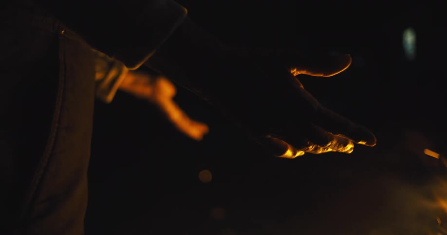 A persons arm stretches out toward a bonfire at night