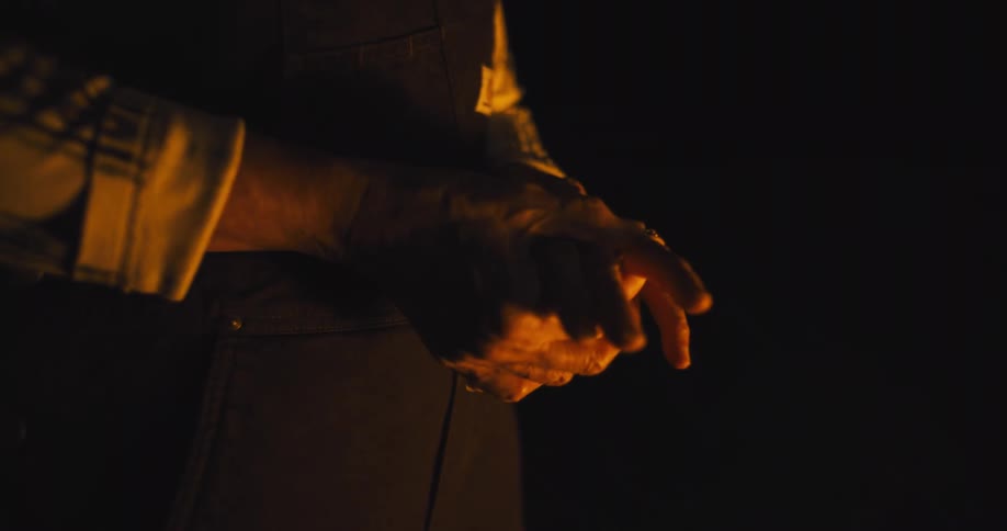 A person holds their hands over a fire burning outdoors at night