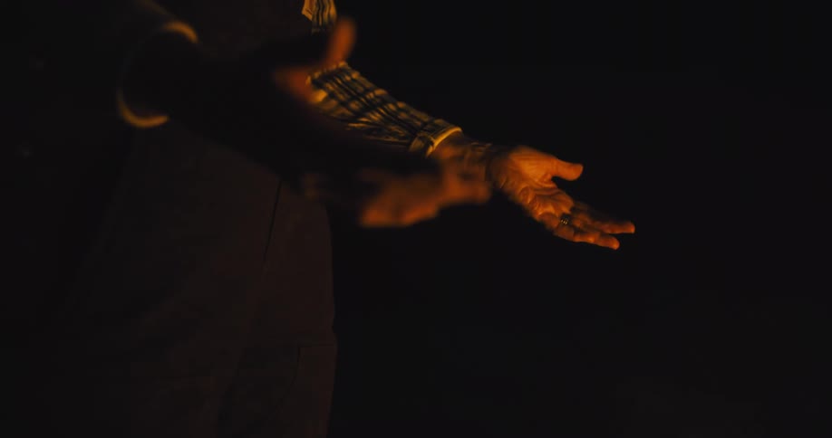 The video shows a person with a longsleeved shirt silhouetted against a dark background with their hands held out sparks of light are seen rising from their open palms and floating upwards