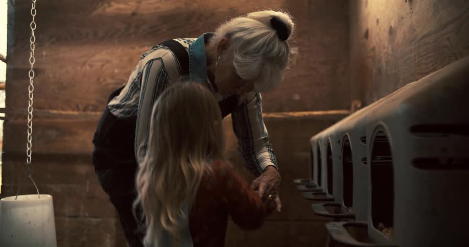 An elderly woman and a young girl collect eggs from a chicken coop