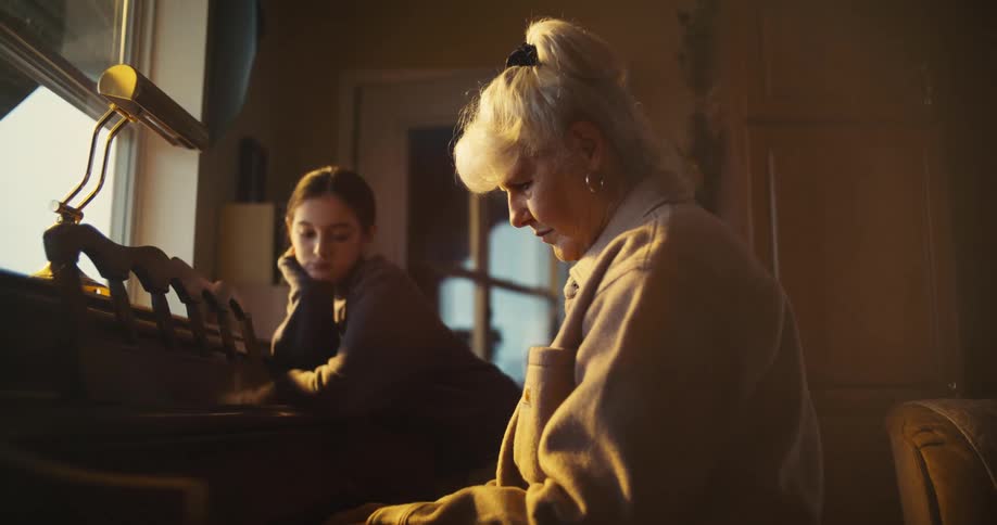 Elderly woman plays piano while a young girl watches beside her