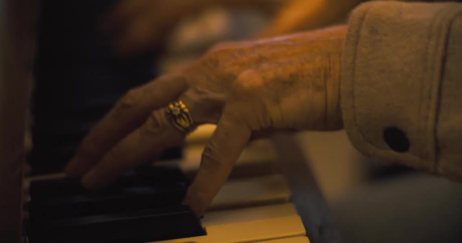 Closeup of elderly hands playing piano keys in soft light