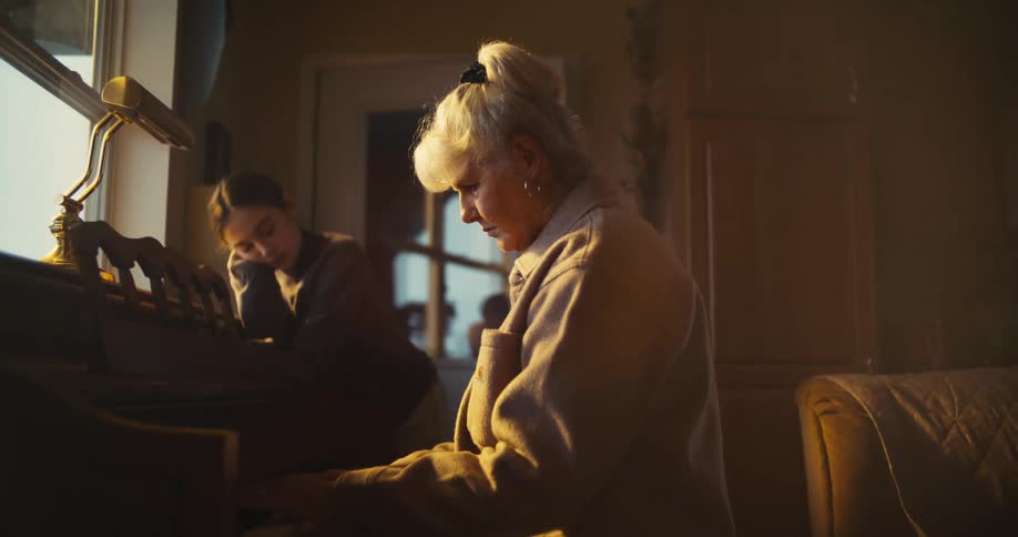 Girl leans against a piano at home while her mother plays