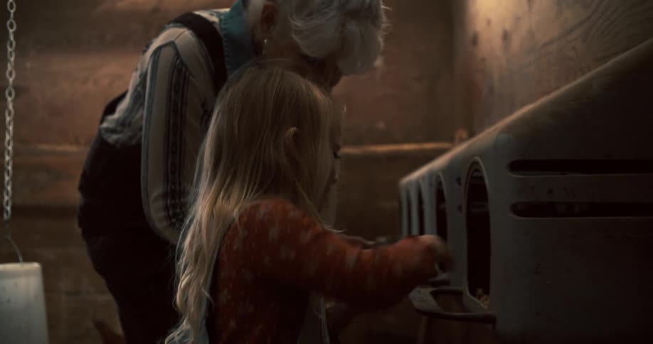 A young girl and an older man in overalls interacting with chickens by a chicken coop with the girl excitedly reaching inside