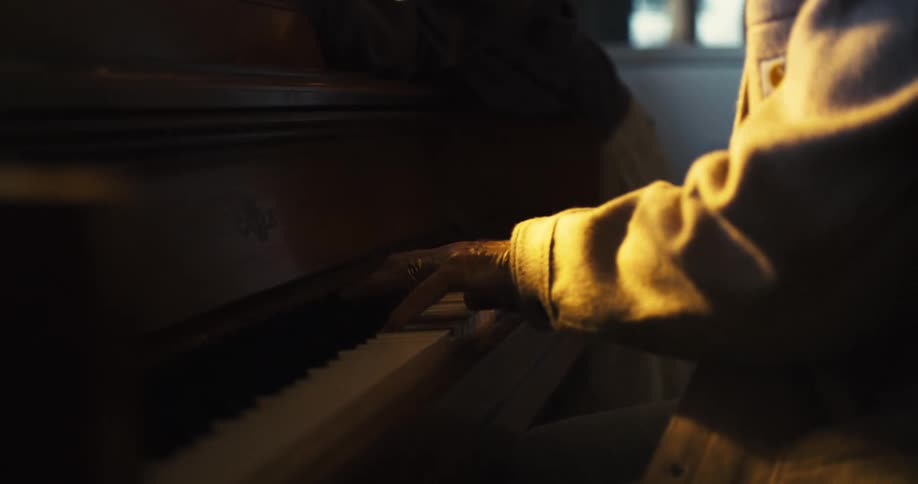 A person wearing a brown jacket plays a grand piano indoors