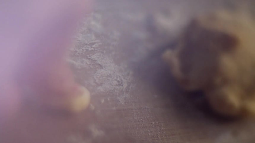 A child's thumb is pressed into a piece of dough