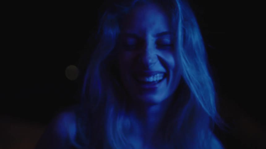 A young blonde woman laughs happily inside a dark room