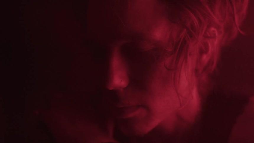 A young woman with blonde hair is seen in a profile shot she is looking down and her face is illuminated with a bright red light