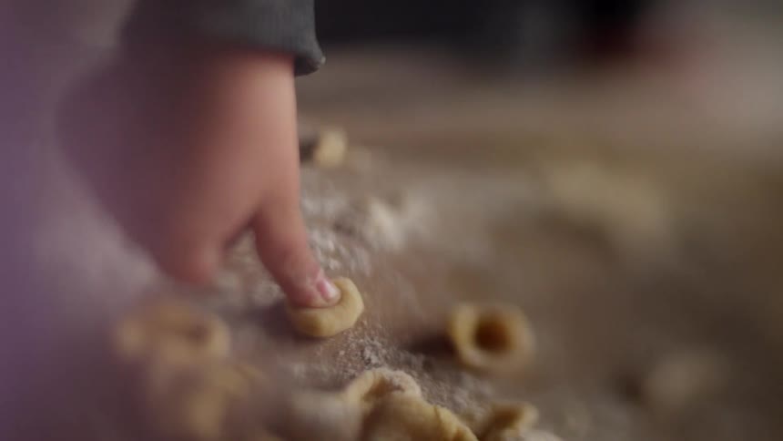 A young child presses pasta on a cutting board