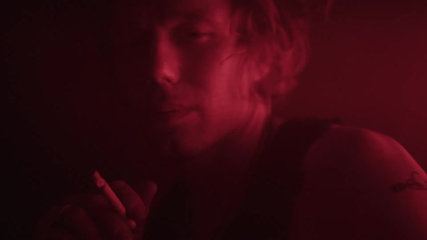 Man smokes in an area dimly lit by colored lighting