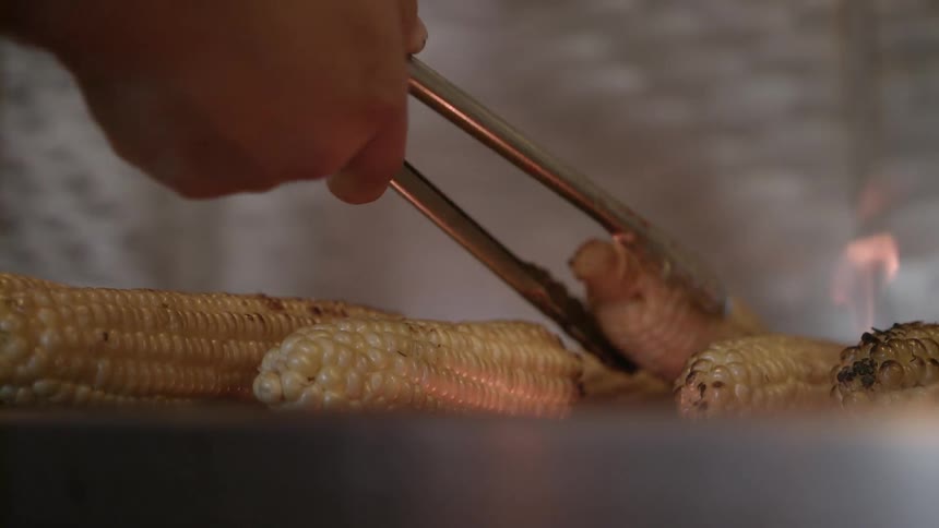 A person is turning some corn on the grill