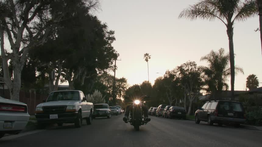A man on a motorcycle riding down the street with headlights on