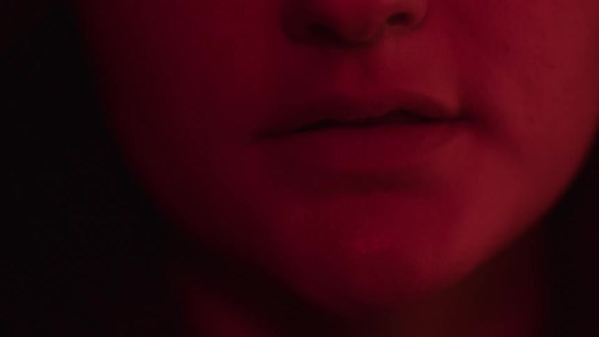 The video is a very tight closeup shot of a persons face starting at their mouth and slowly moving up the person is illuminated by a deep red light the shot ends with their eyes visible
