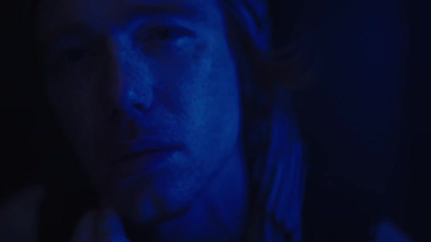 Person with rings on their finger resting their face under intense blue lighting