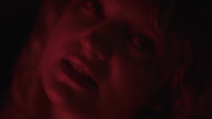 A close view shows a woman with her head tilted back her mouth slightly open and her teeth visible with a deep red light shining on her face from below