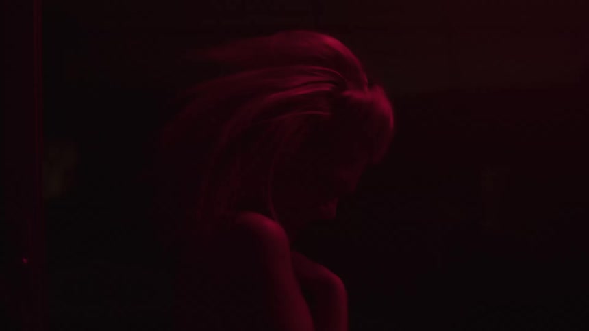 A woman in a dark room lit only by a dim red light dancing while smiling and shaking her head and hair